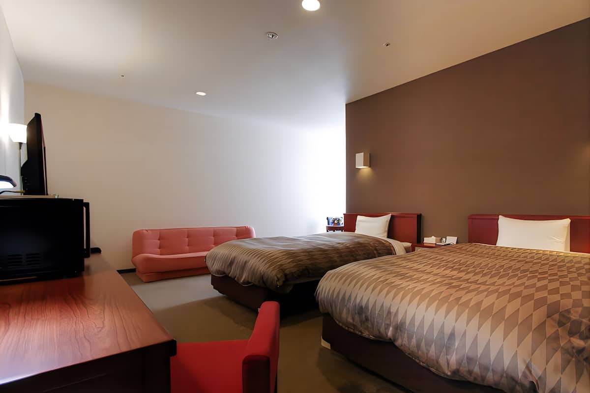 Ein Hotelzimmer mit zwei Betten, einem Schreibtisch, einem Fernseher und einem roten Sessel.