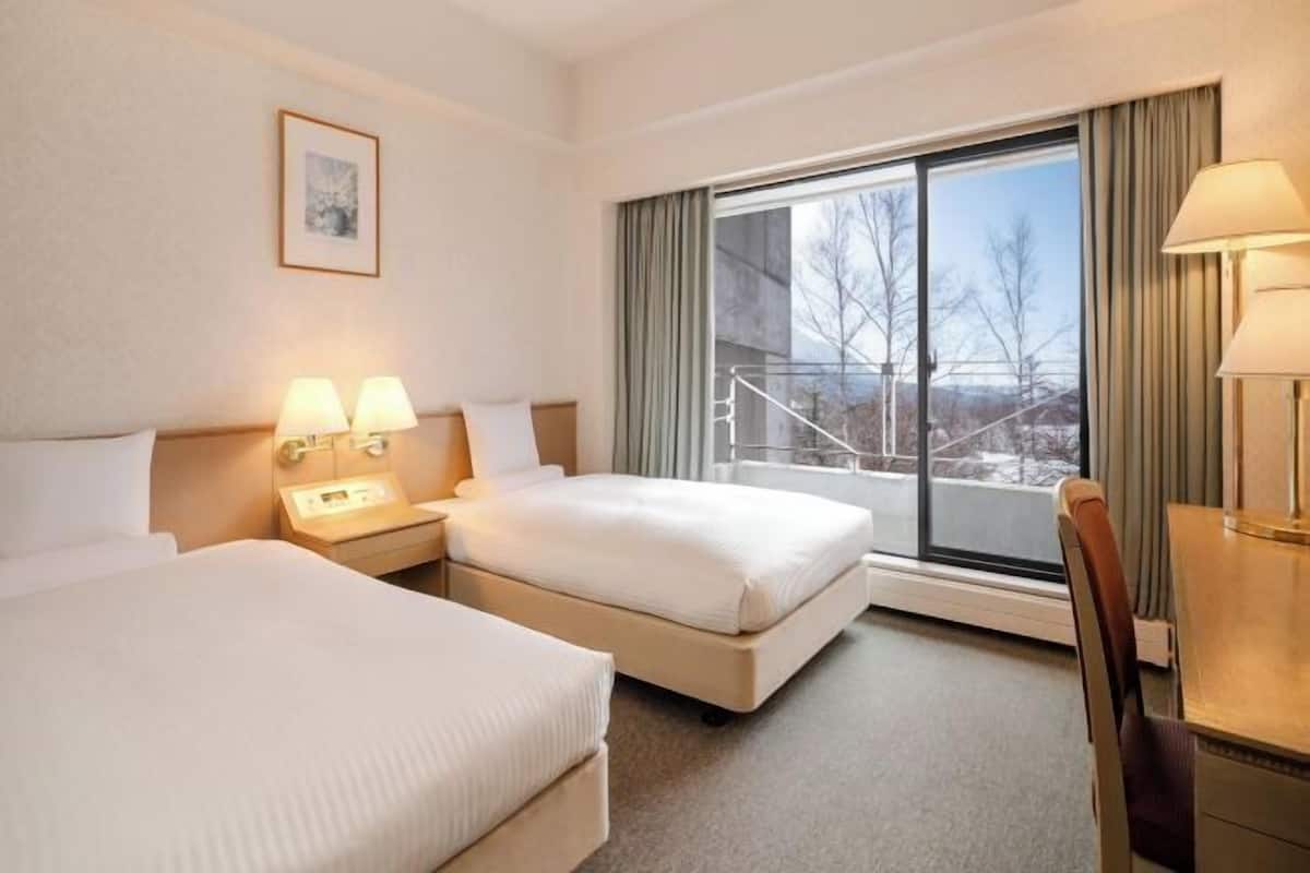 A hotel room with two beds, a desk, and a large window with a view of a snowy landscape.