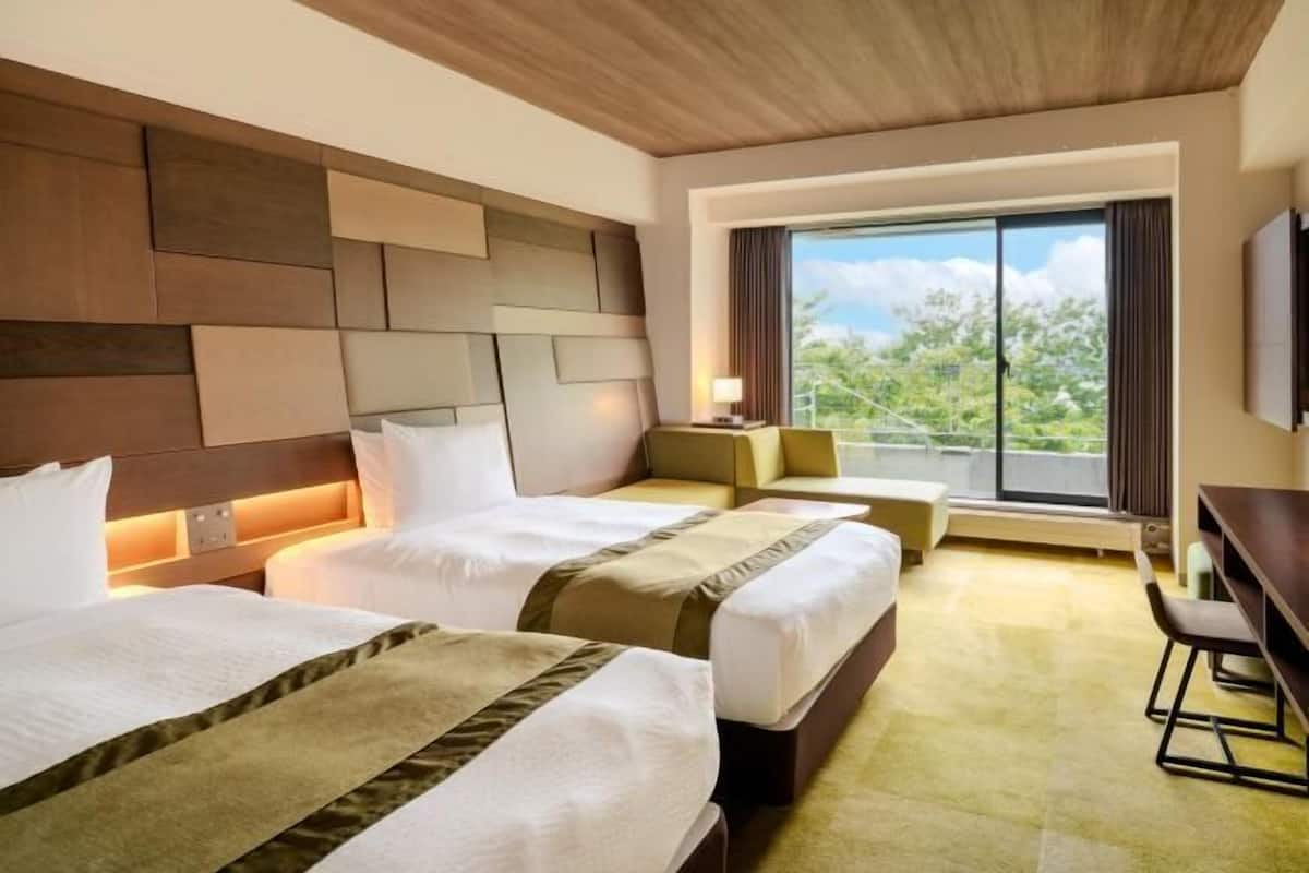 A hotel room with two beds, a desk, a chair, and a large window with a view.