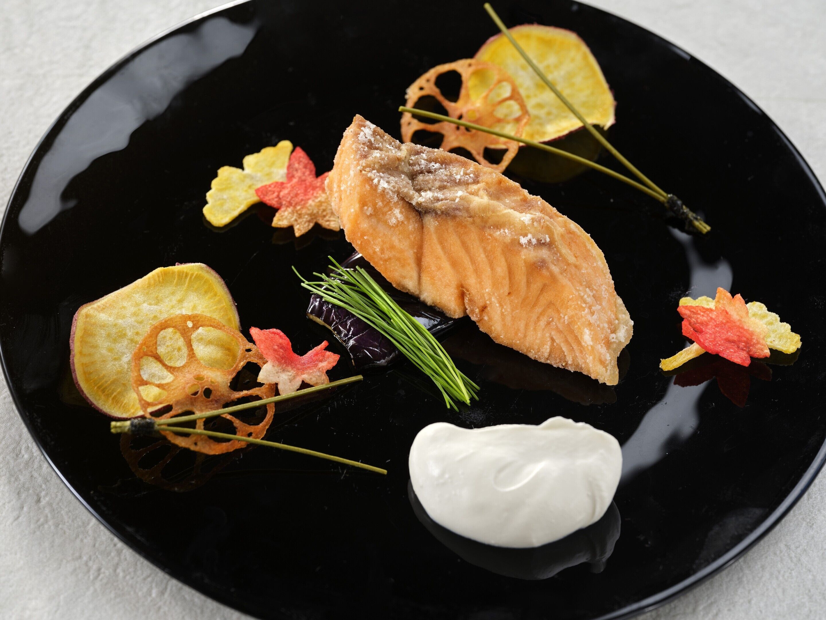 A black plate with a piece of salmon, some vegetables, and a dollop of cream.