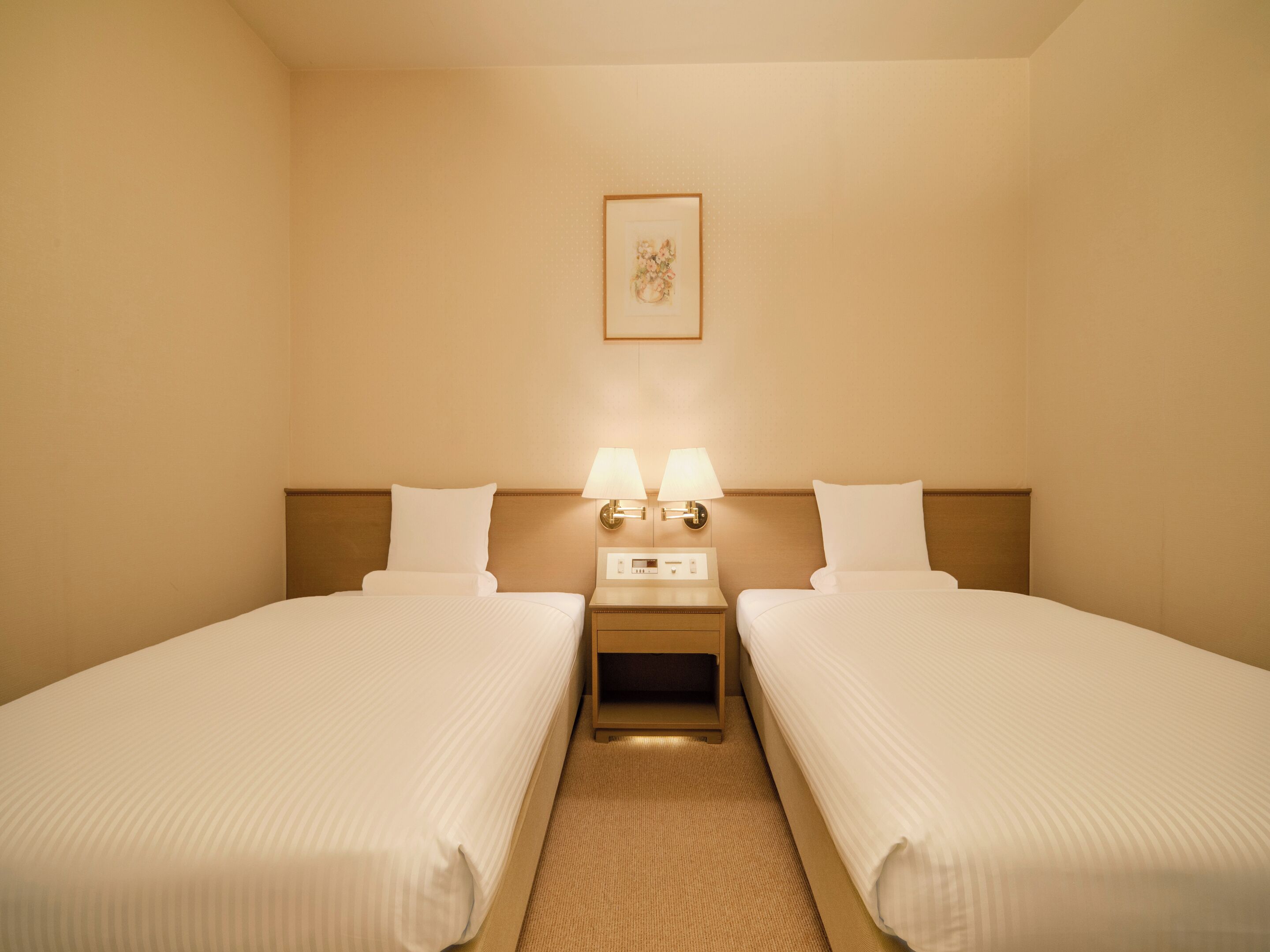 Een hotelkamer met twee bedden, een nachtkastje met lampen en een lijst aan de muur.