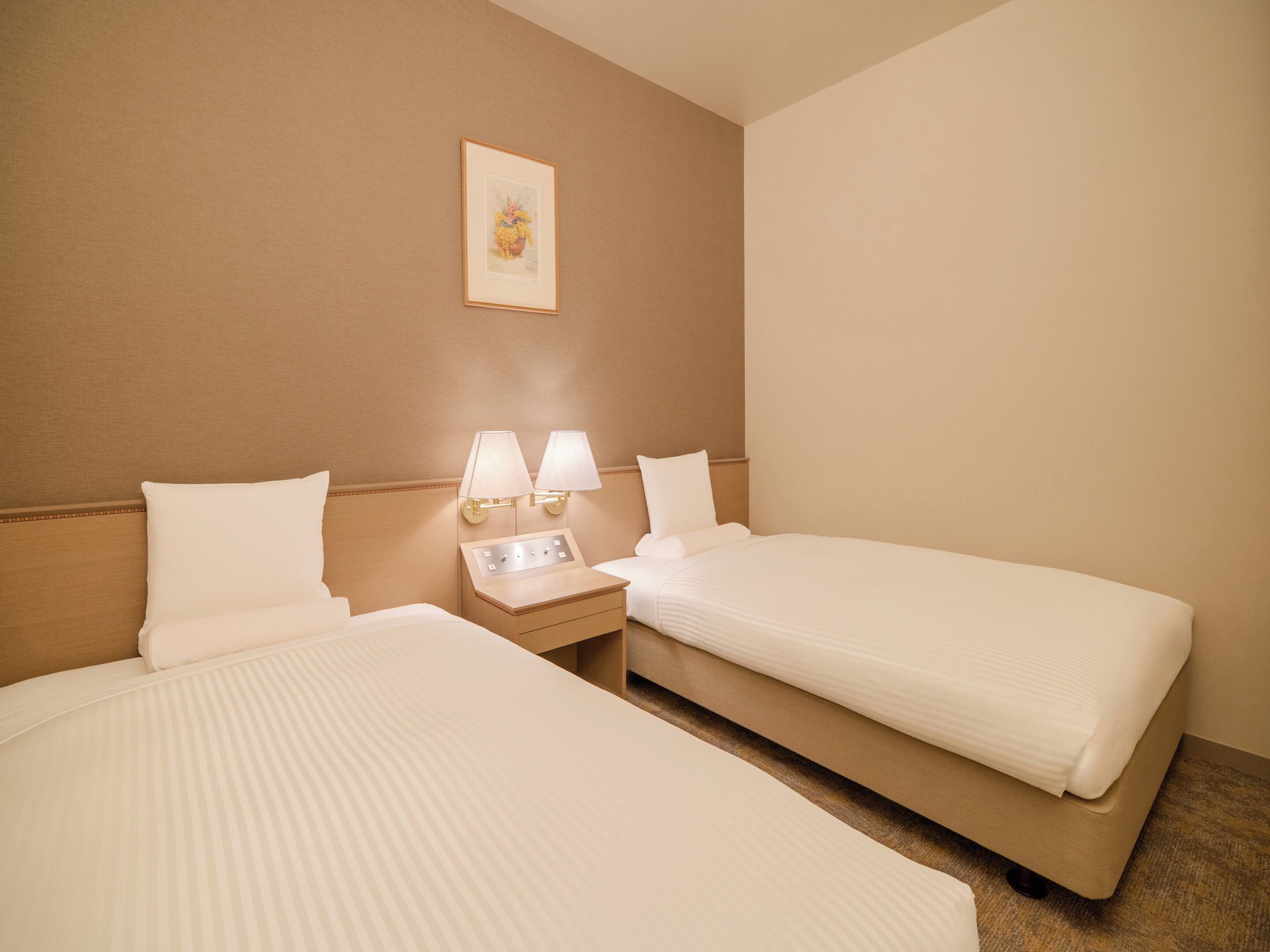 Une chambre d’hôtel avec deux lits, une table de chevet avec des lampes et un tableau encadré au mur.