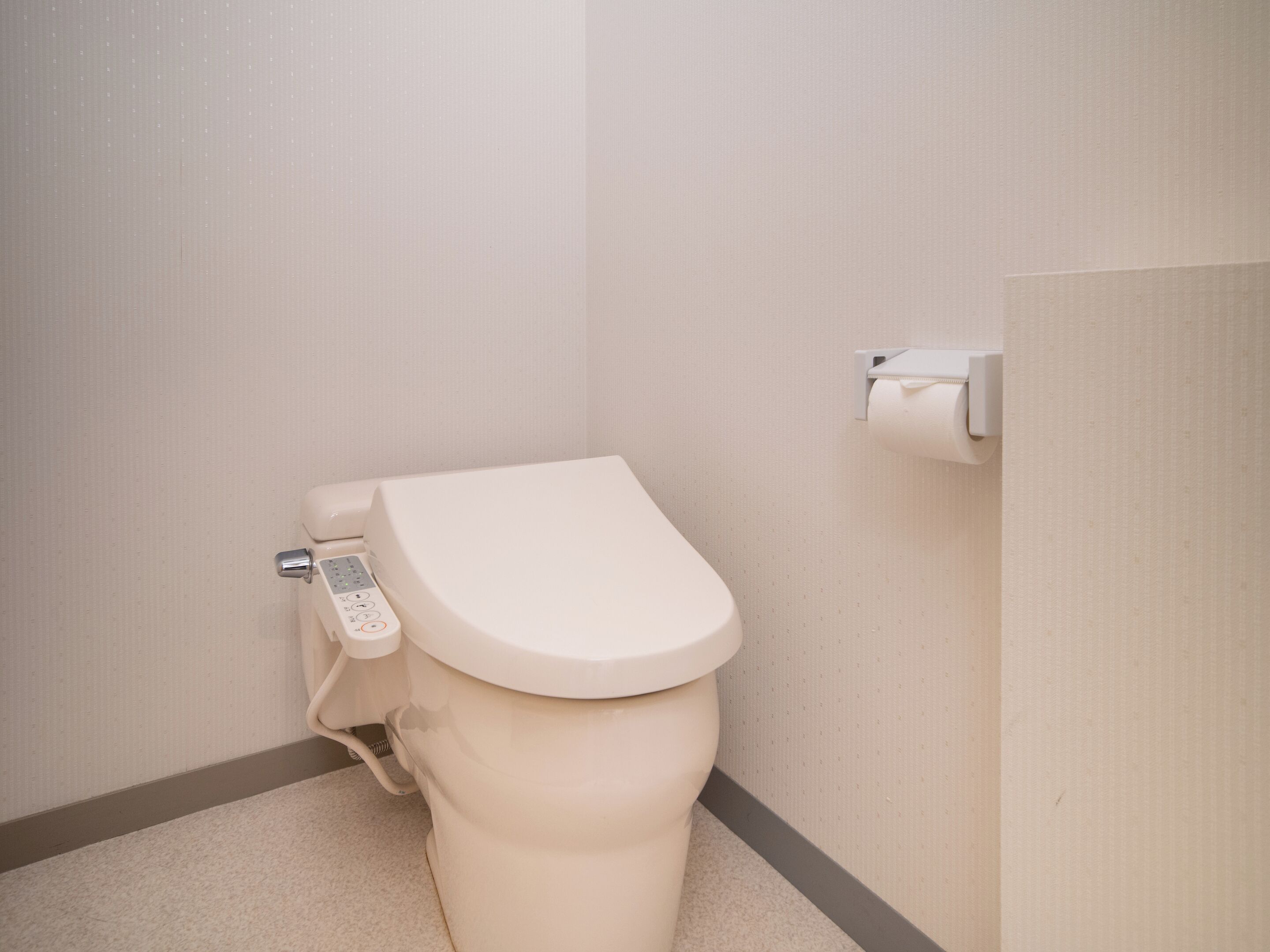 A modern toilet with a control panel, a toilet paper holder, and a plain wall.