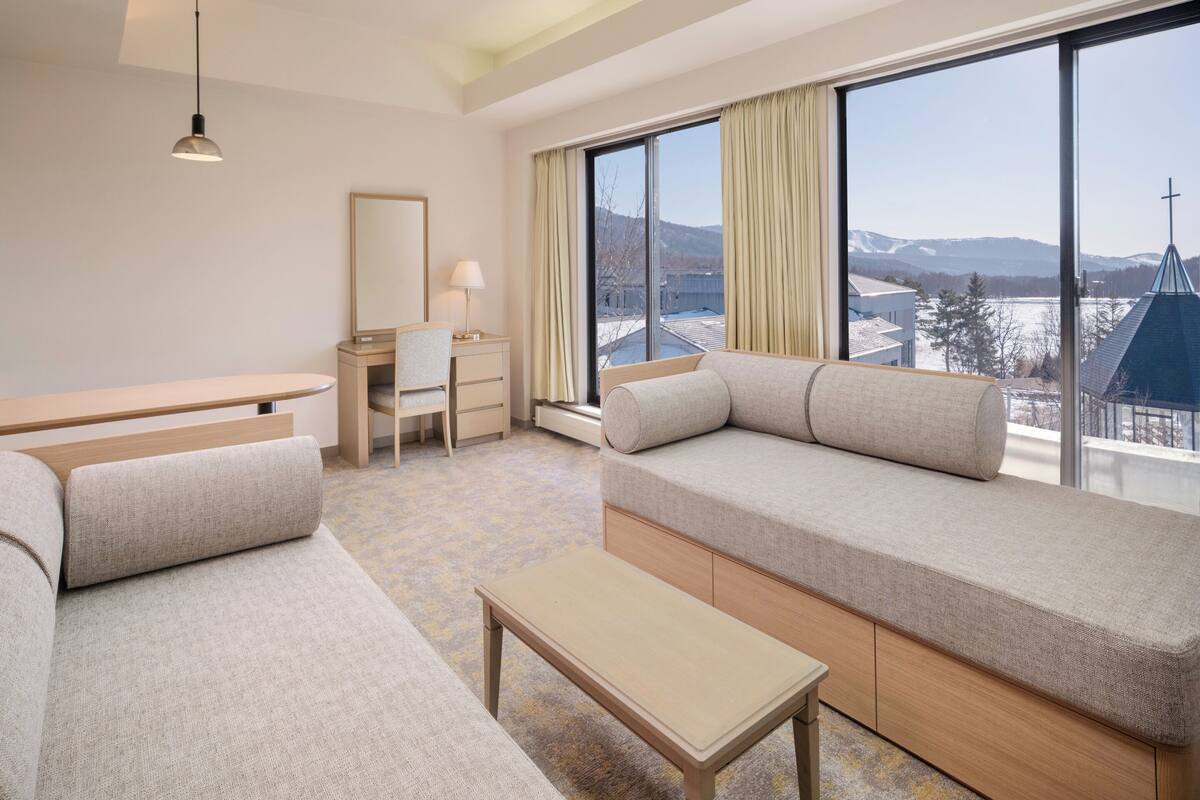 Ein modernes Hotelzimmer mit großem Fenster, einer Couch, einem Schreibtisch und einer Lampe.