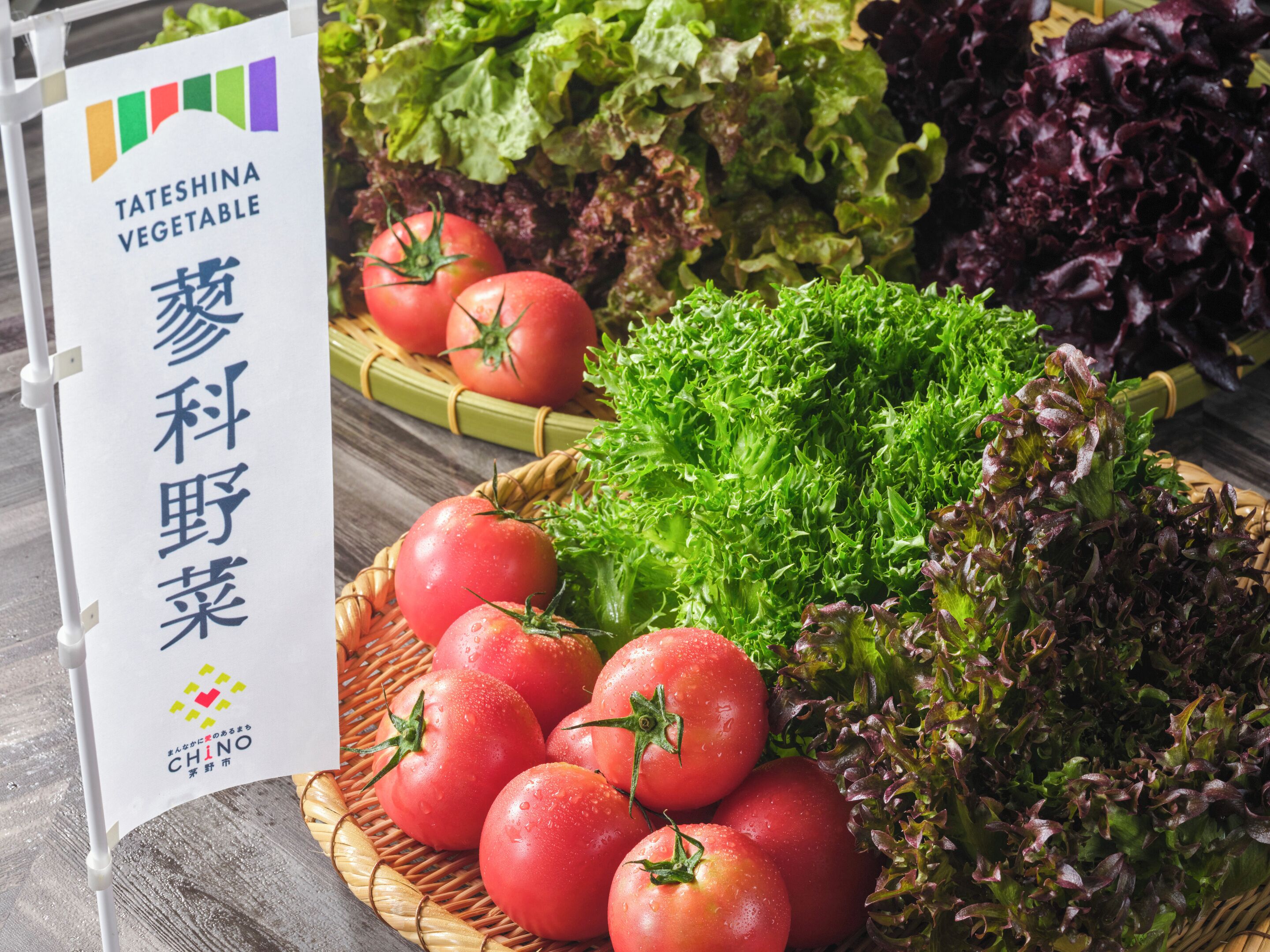 A display of fresh vegetables including tomatoes and leafy greens, with a sign indicating 'TATESHINA VEGETABLE' and 'CHINO' branding.