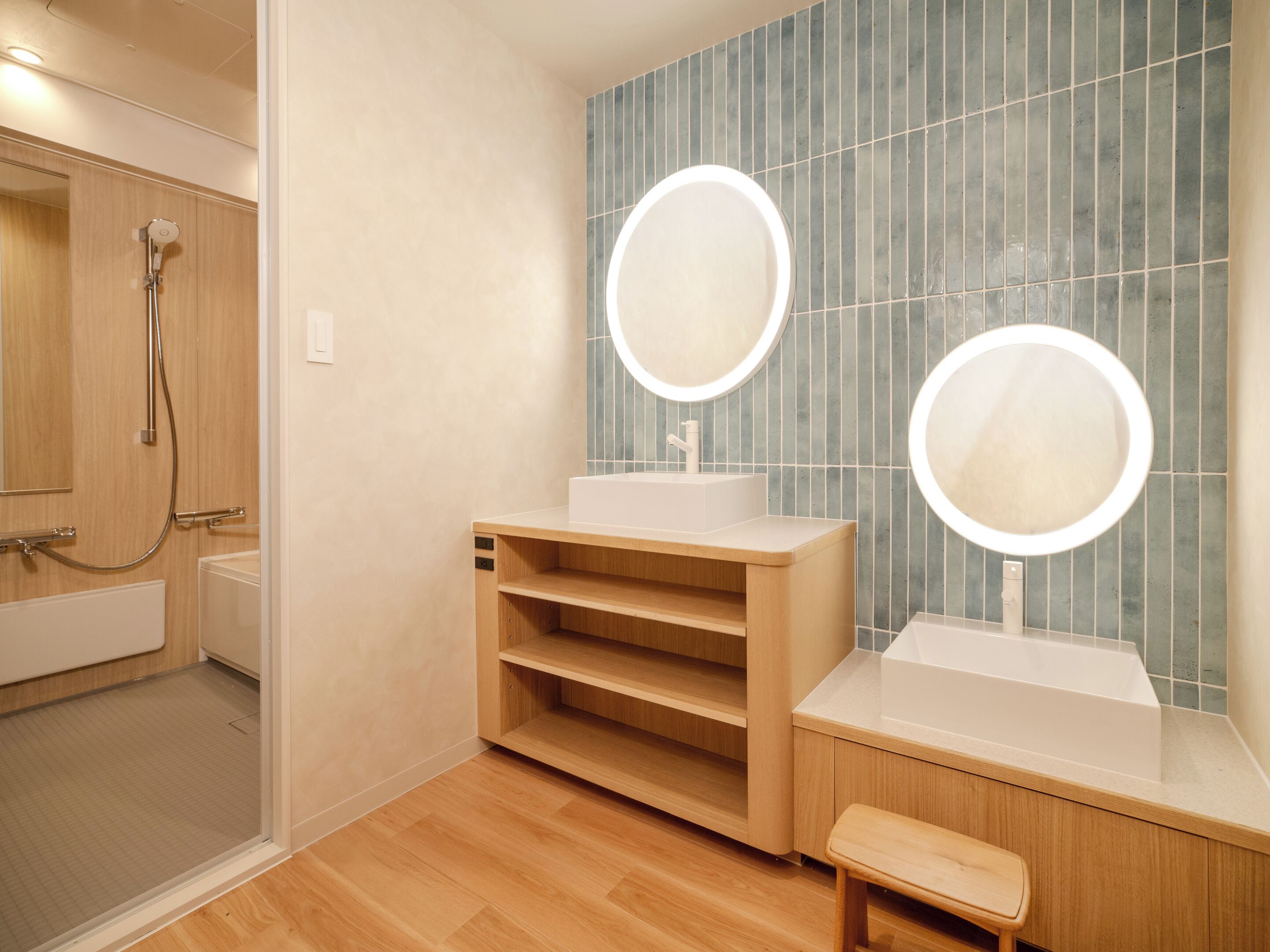 A modern bathroom with a shower, two sinks with illuminated mirrors, and a wooden vanity.