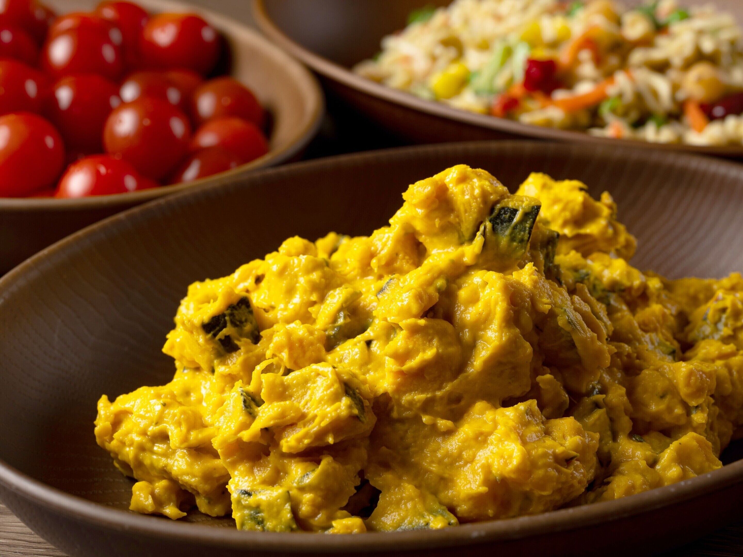 A bowl of yellow curry with visible green herbs, a bowl of cherry tomatoes, and a plate of mixed vegetables.