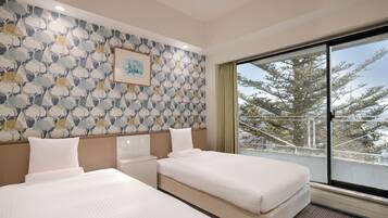 A hotel room with two beds, a large window with a view of trees, a patterned wallpaper, and a framed picture on the wall.