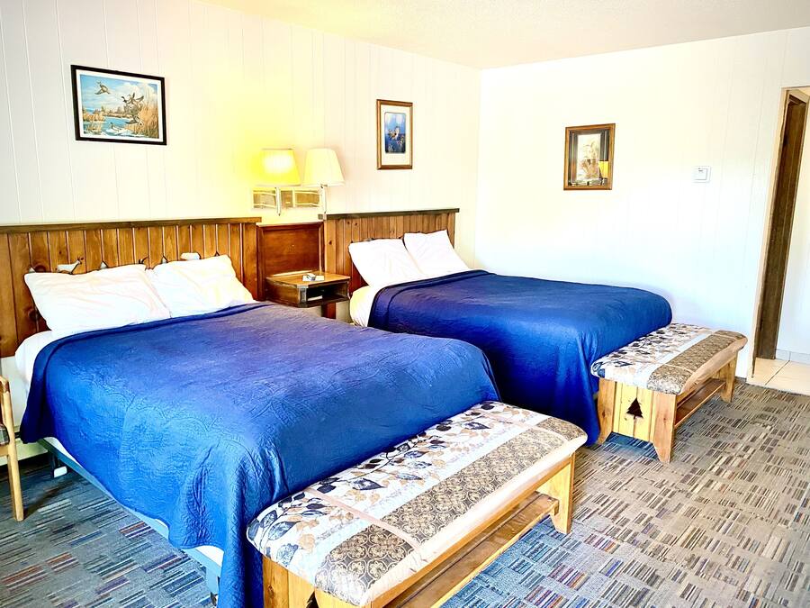 Een hotelkamer met twee bedden, een bankje, een nachtkastje en een lamp.