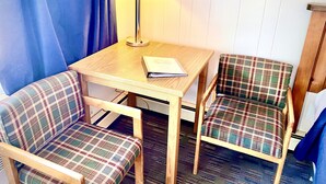 A small room with a wooden table, two plaid chairs, a lamp, and a book on the table. - Forest Lake Motel (Grand Rapids)
