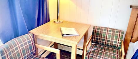 A small room with a wooden table, two plaid chairs, a lamp, and a book on the table.