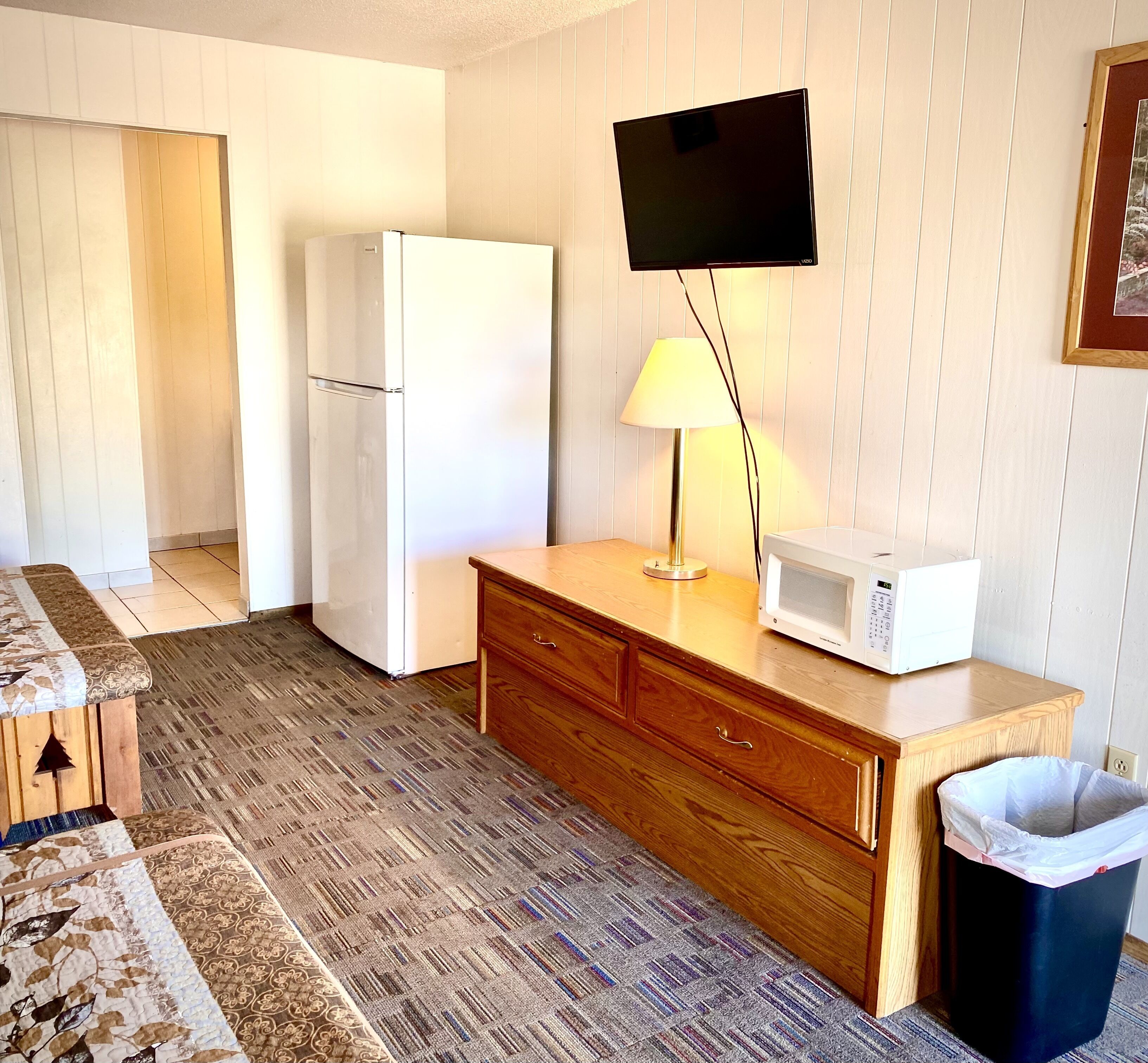 A compact kitchen with a refrigerator, microwave, wooden cabinet, and a trash bin.