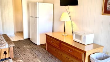 A compact kitchen with a refrigerator, microwave, wooden cabinet, and a trash bin.