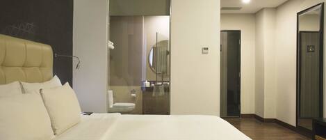 Une chambre d’hôtel avec un grand lit, une salle de bain dotée d’une douche à parois de verre et un miroir au mur.