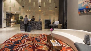 A hotel reception area with a marble counter, a reception desk, a sofa, and a patterned rug. - Liberty Hotel Thamrin Jakarta (Jakarta)