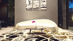 A modern room with a large, curved white sofa, a patterned carpet, and a unique chandelier. - Liberty Hotel Thamrin Jakarta (Jakarta)