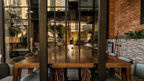 A conference room with a large wooden table surrounded by chairs, a glass partition, and a brick wall. - Liberty Hotel Thamrin Jakarta (Jakarta)