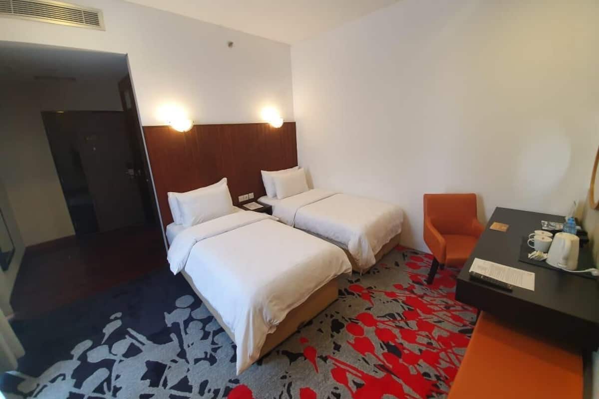 A hotel room with two beds, a desk with a chair, and a patterned carpet.
