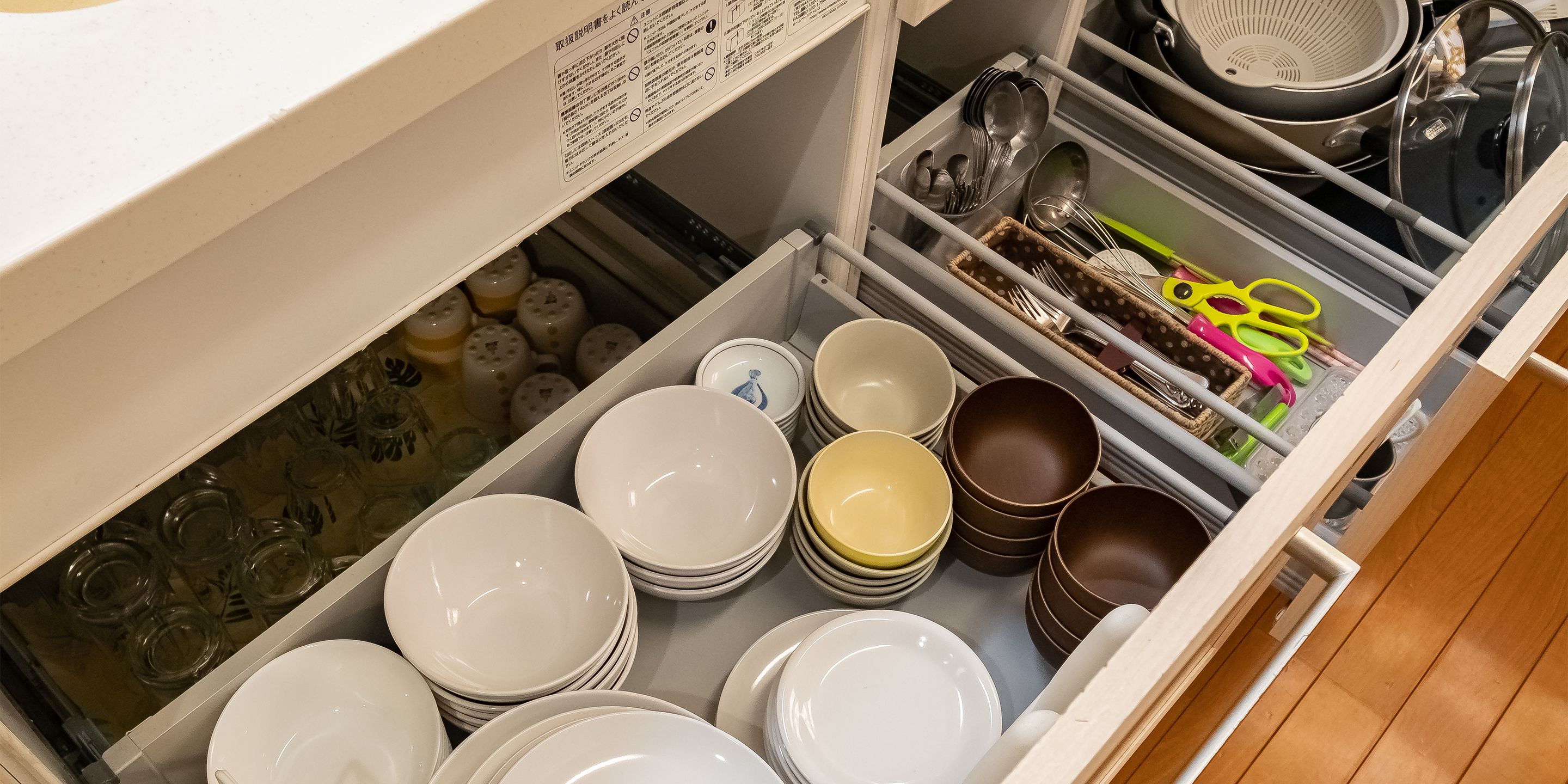 A kitchen drawer with neatly stacked plates and bowls, a colander, and a pair of scissors.