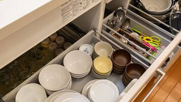 A kitchen drawer with neatly stacked plates and bowls, a colander, and a pair of scissors.