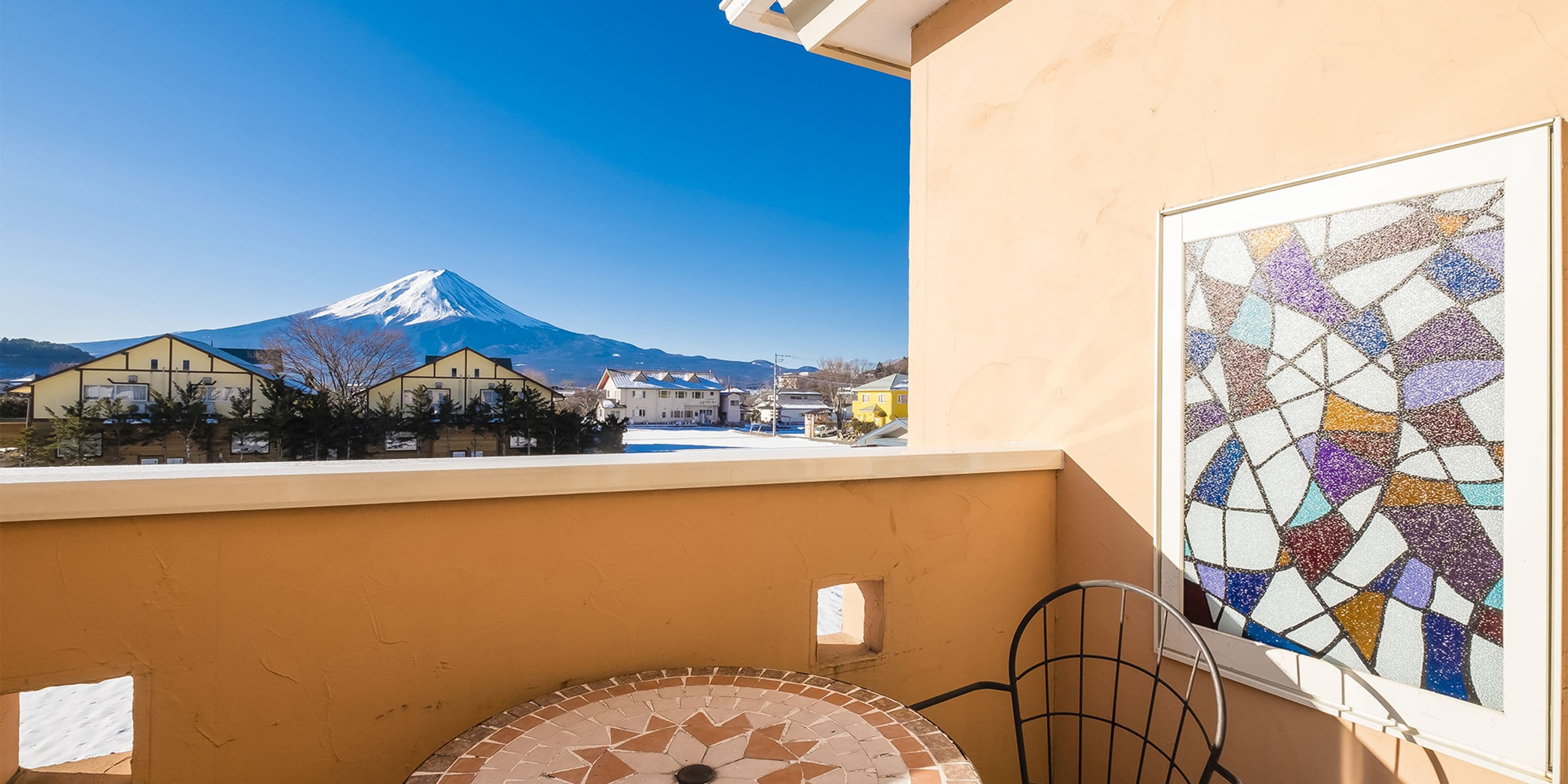Un balcon offrant une vue sur une montagne enneigée, un sol carrelé et une œuvre d’art en mosaïque.