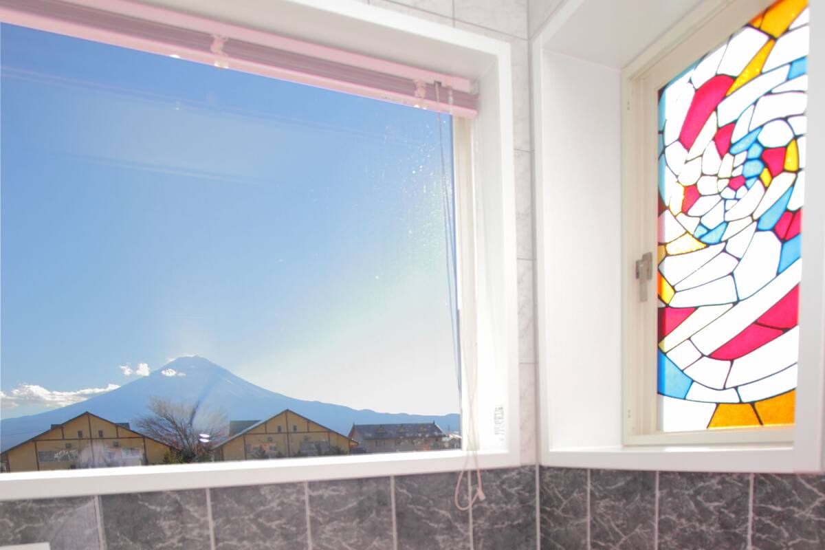 A bathroom with a bathtub filled with pink water, a window with a view of a mountain, and a stained glass window.