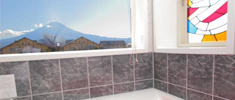 A bathroom with a bathtub filled with pink water, a window with a view of a mountain, and a stained glass window.