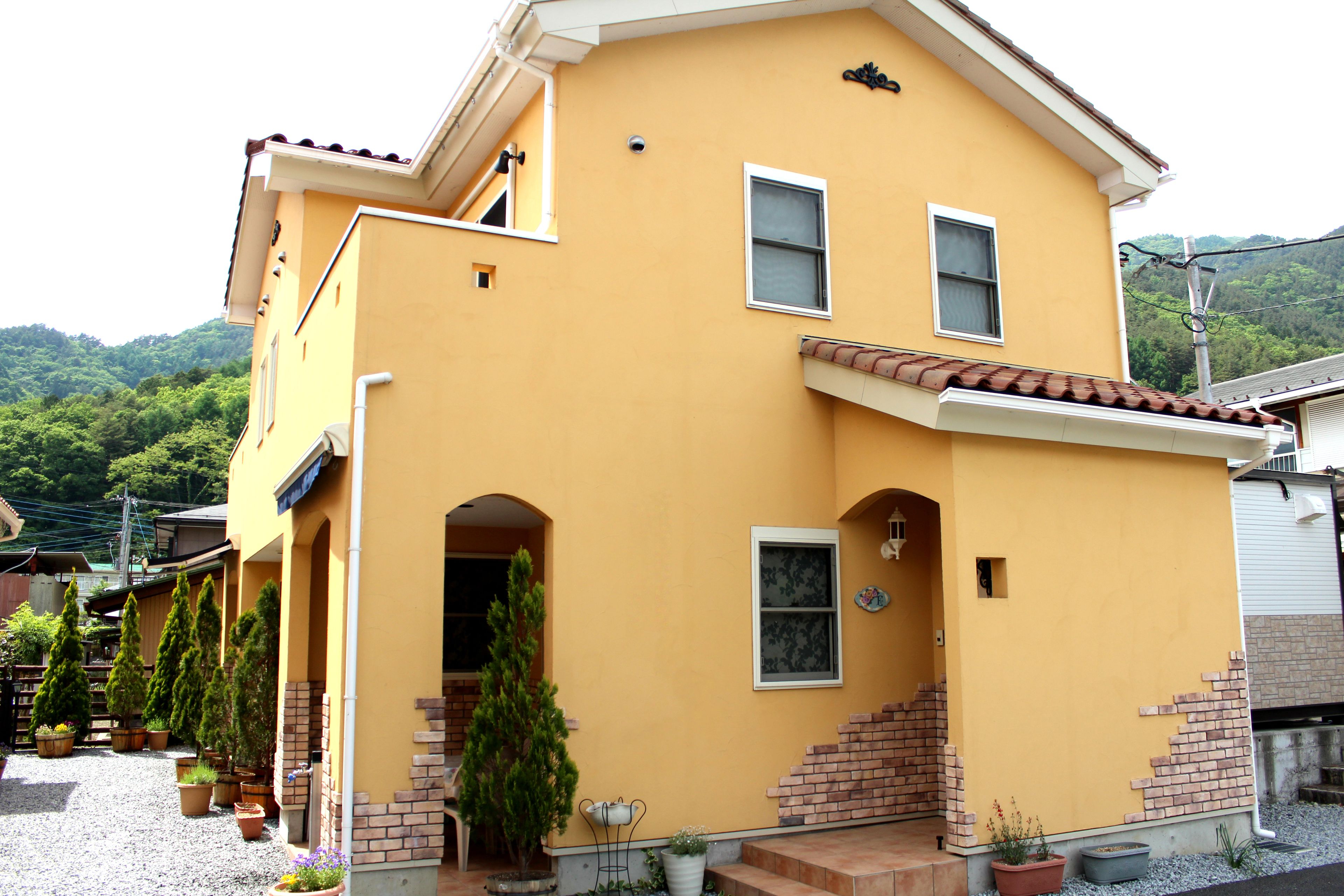 A two-story house with a yellow exterior, a brick staircase, and potted plants.