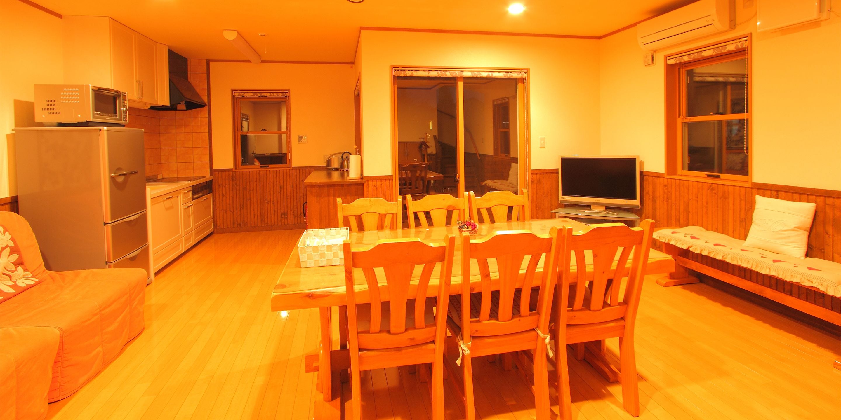 Un espacio habitable compacto con una mesa de comedor, sillas, un sofá, un televisor y una zona de cocina con microondas.