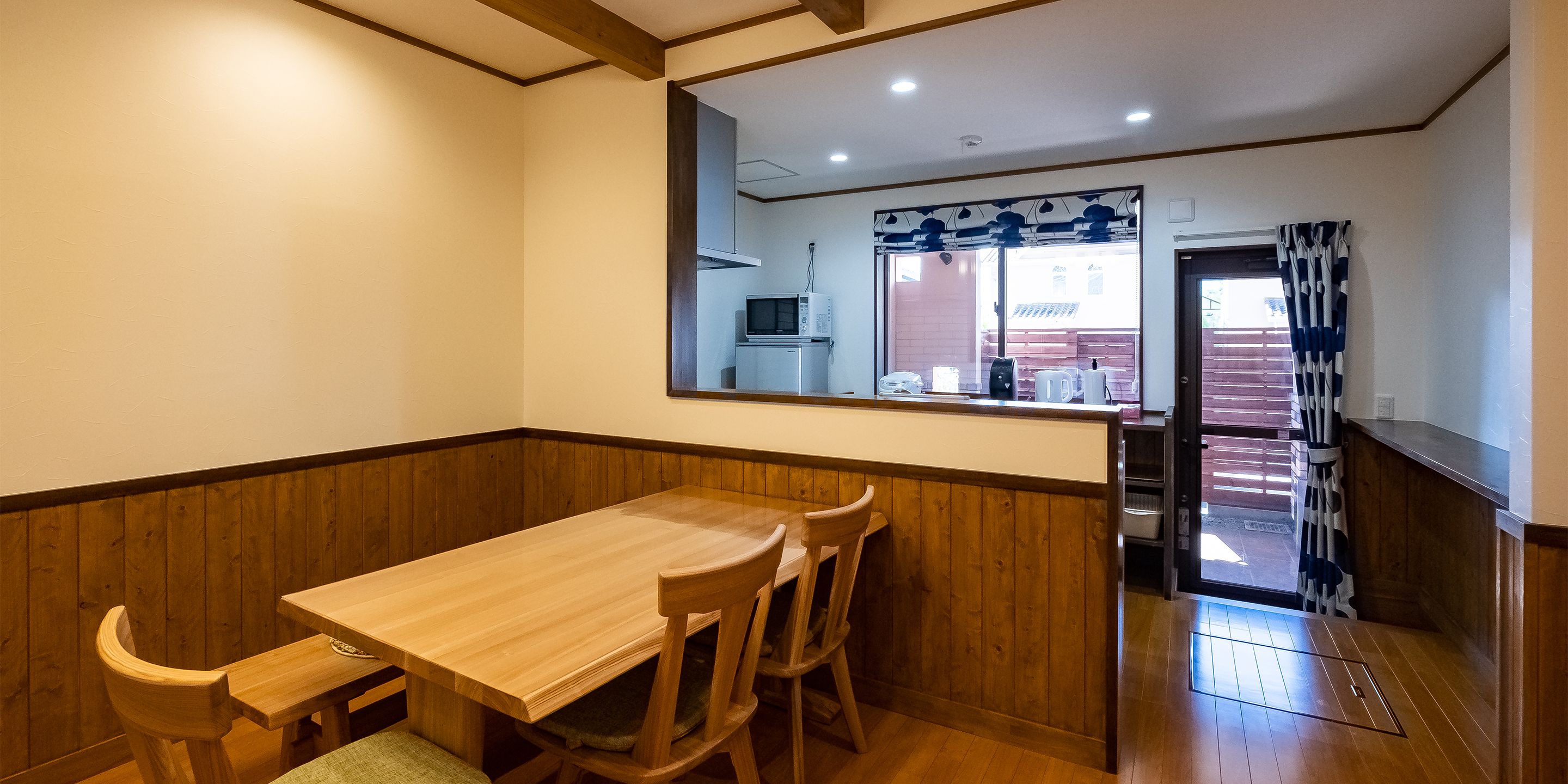 A dining area with a wooden table and chairs, a view of the kitchen, and a wooden floor.