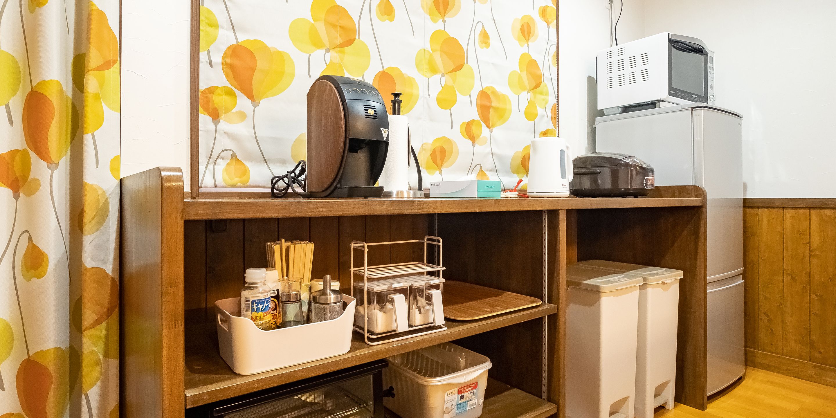 A kitchen area with a microwave, coffee maker, and various kitchen utensils on the counter. There are storage bins and shelves below the counter.
