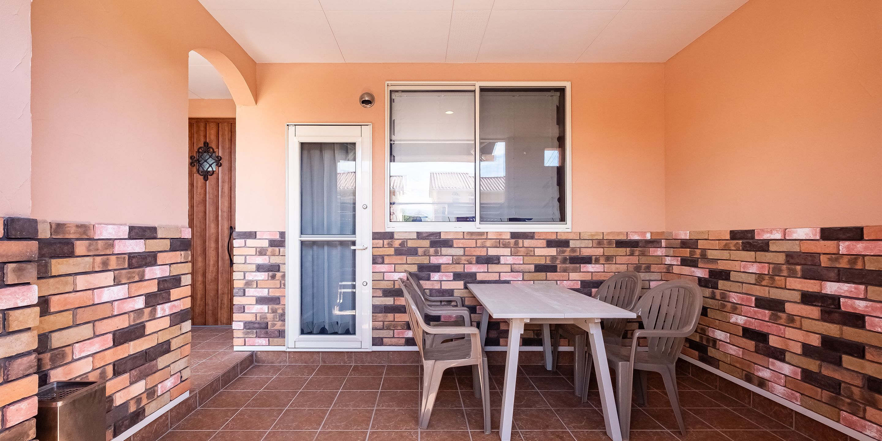 Un pequeño patio con una mesa, sillas, una puerta corrediza de vidrio y un muro con diseño de ladrillo.