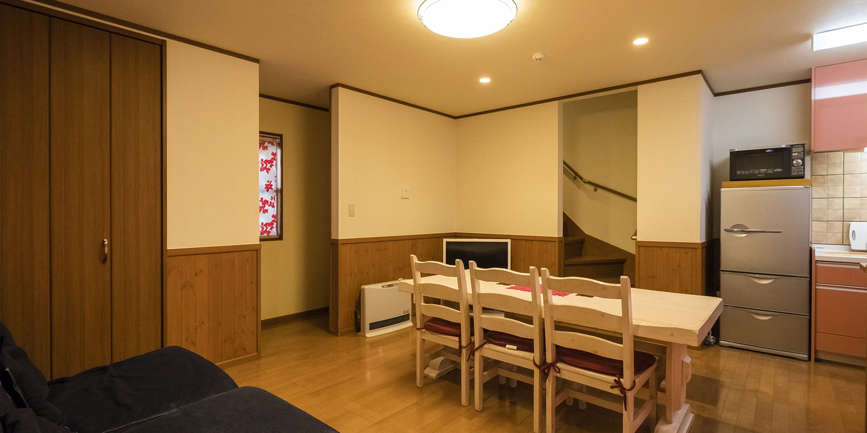 A compact kitchen with a dining table and chairs, a refrigerator, and a microwave.