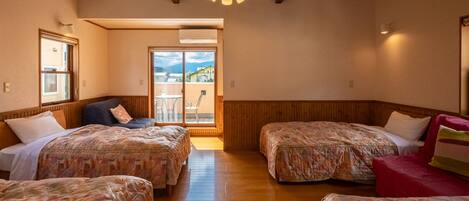 Habitación con dos camas, un sofá y puerta corrediza de cristal que da a un balcón exterior.