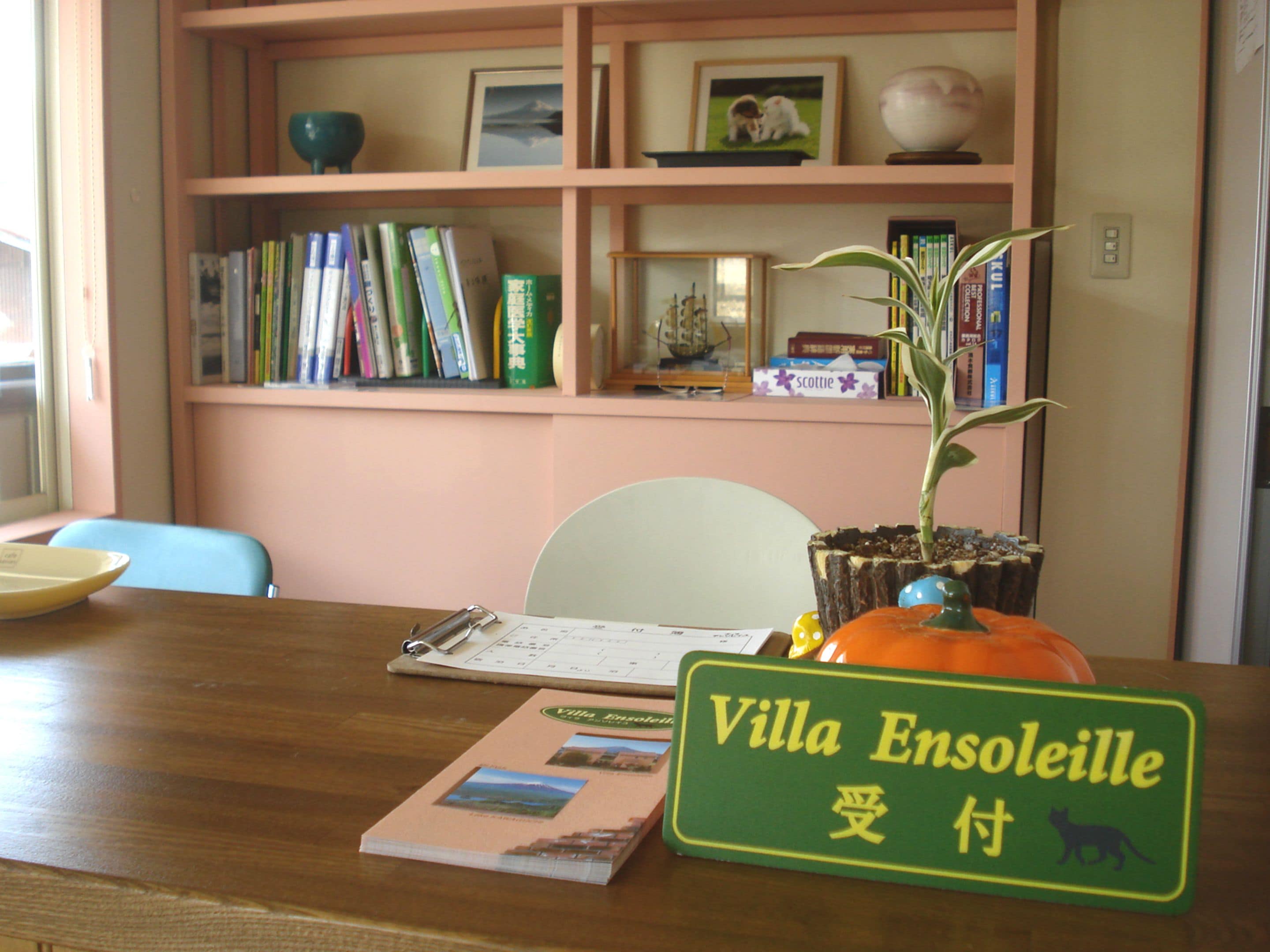 A wooden table with a calendar, a sign reading "Villa Ensoleille," a notebook, and a potted plant.