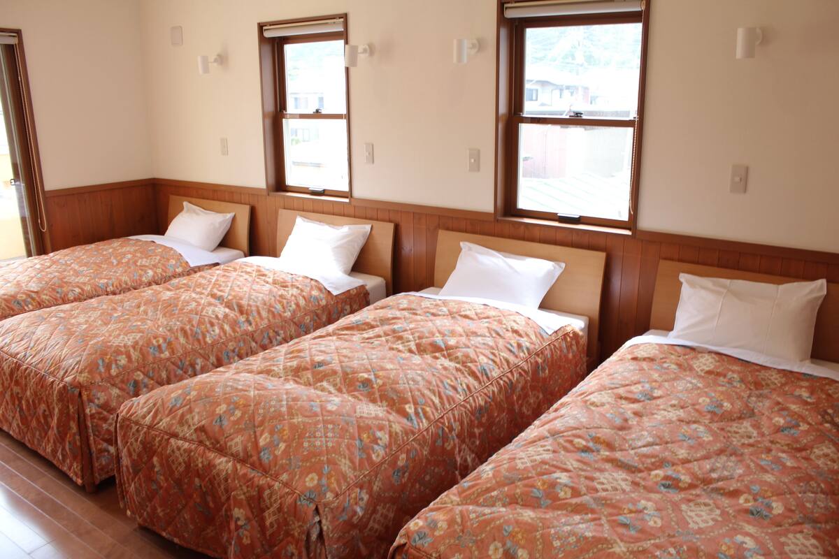A hotel room with three beds arranged in a row, each with a wooden headboard and white bedding.