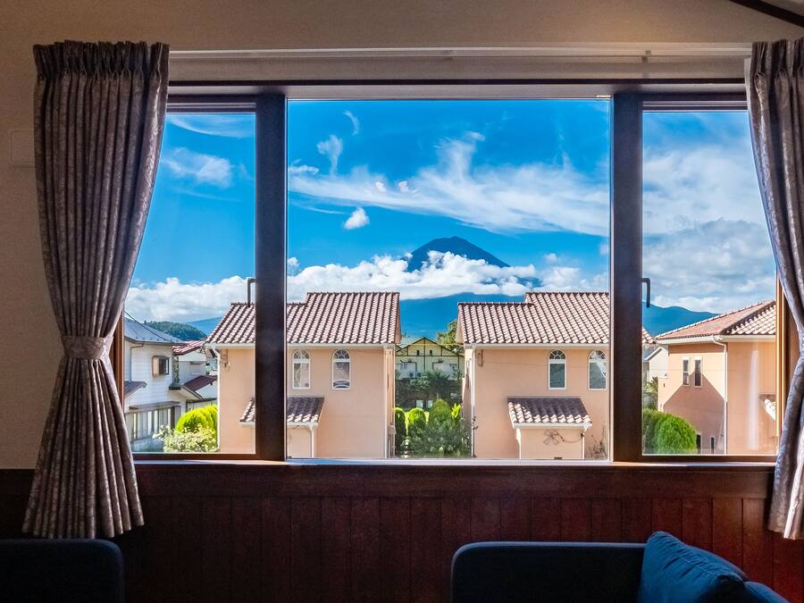 A room with a large window overlooking a residential area, featuring a view of houses and a mountain.