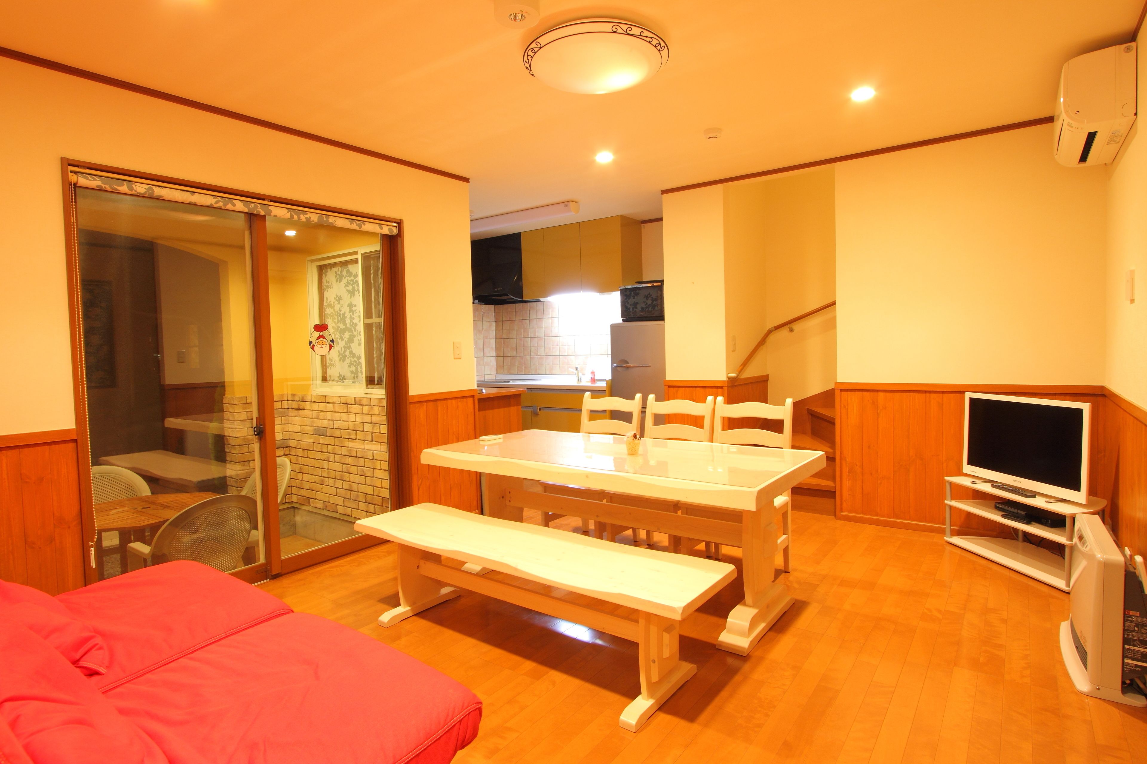 A compact living space with a dining table, bench, TV, and a sliding glass door leading to a balcony.