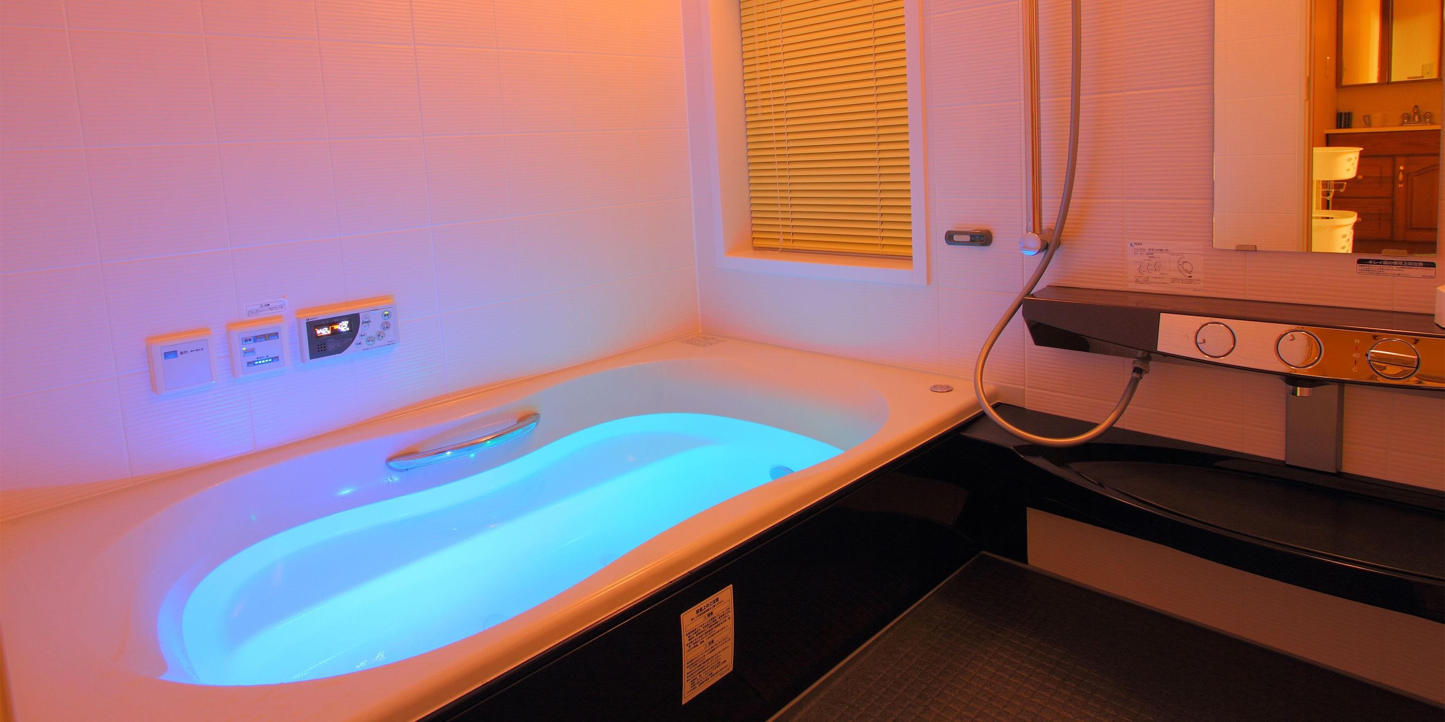 Une salle de spa équipée d’un bain à remous chauffé, d’un panneau de commande et d’une fenêtre avec stores.