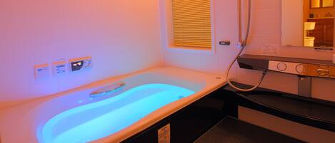 Une salle de spa équipée d’un bain à remous chauffé, d’un panneau de commande et d’une fenêtre avec stores.