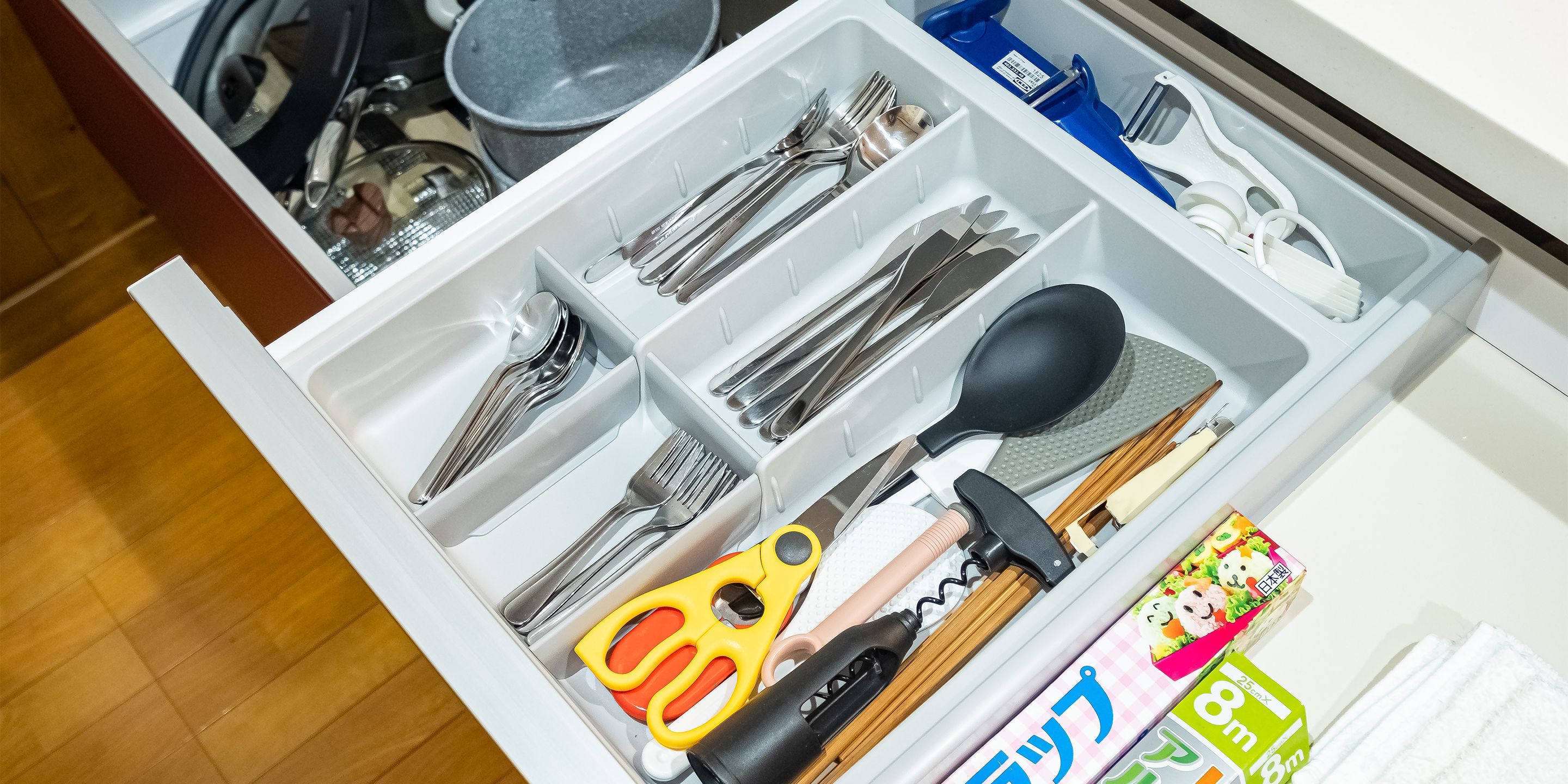 A drawer with compartments containing various kitchen utensils, scissors, and a box of tissues.