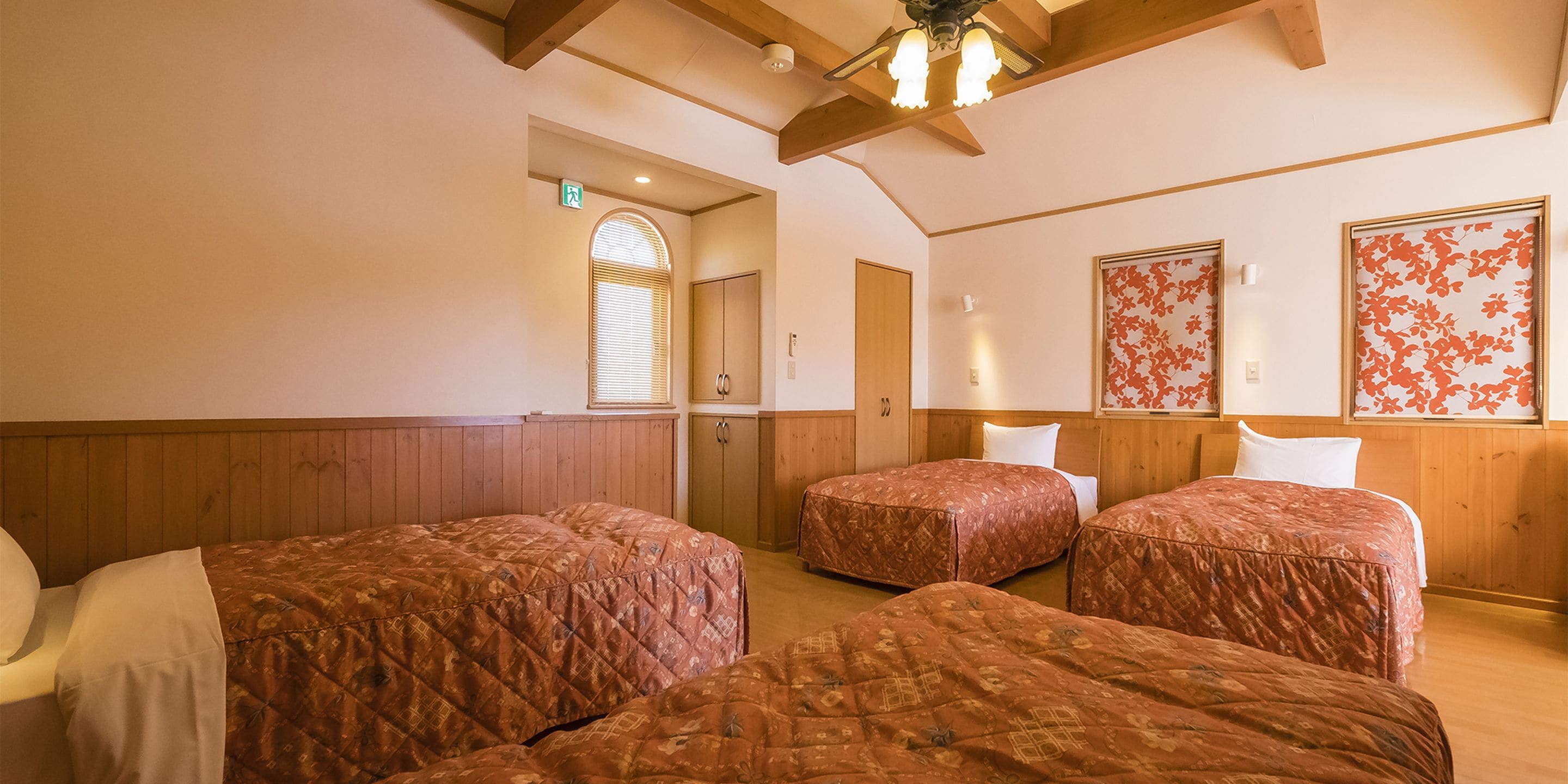 A room with three beds, wooden paneling, a ceiling fan, and floral wall decorations.