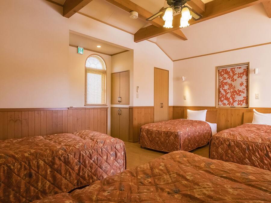 A room with three beds, wooden paneling, a ceiling fan, and floral wall decorations.