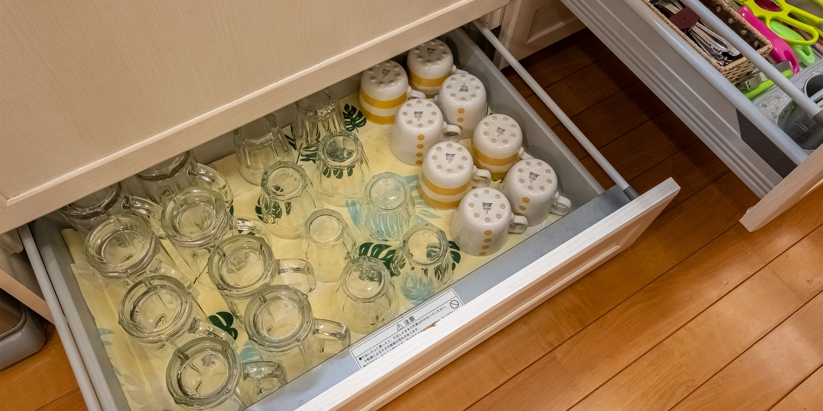 A drawer with various glass containers and ceramic mugs.