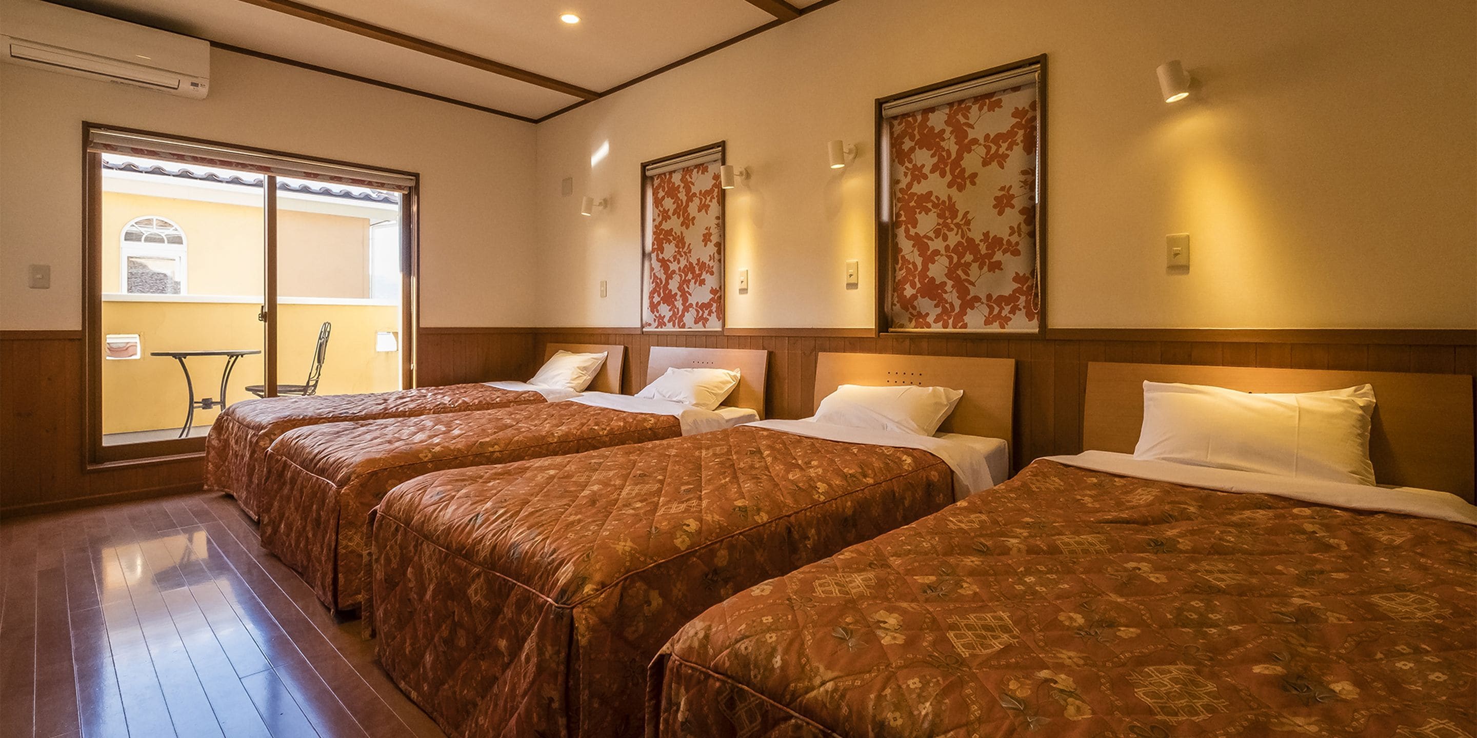 Ein Hotelzimmer mit vier Betten, Holzboden und Blick ins Freie.