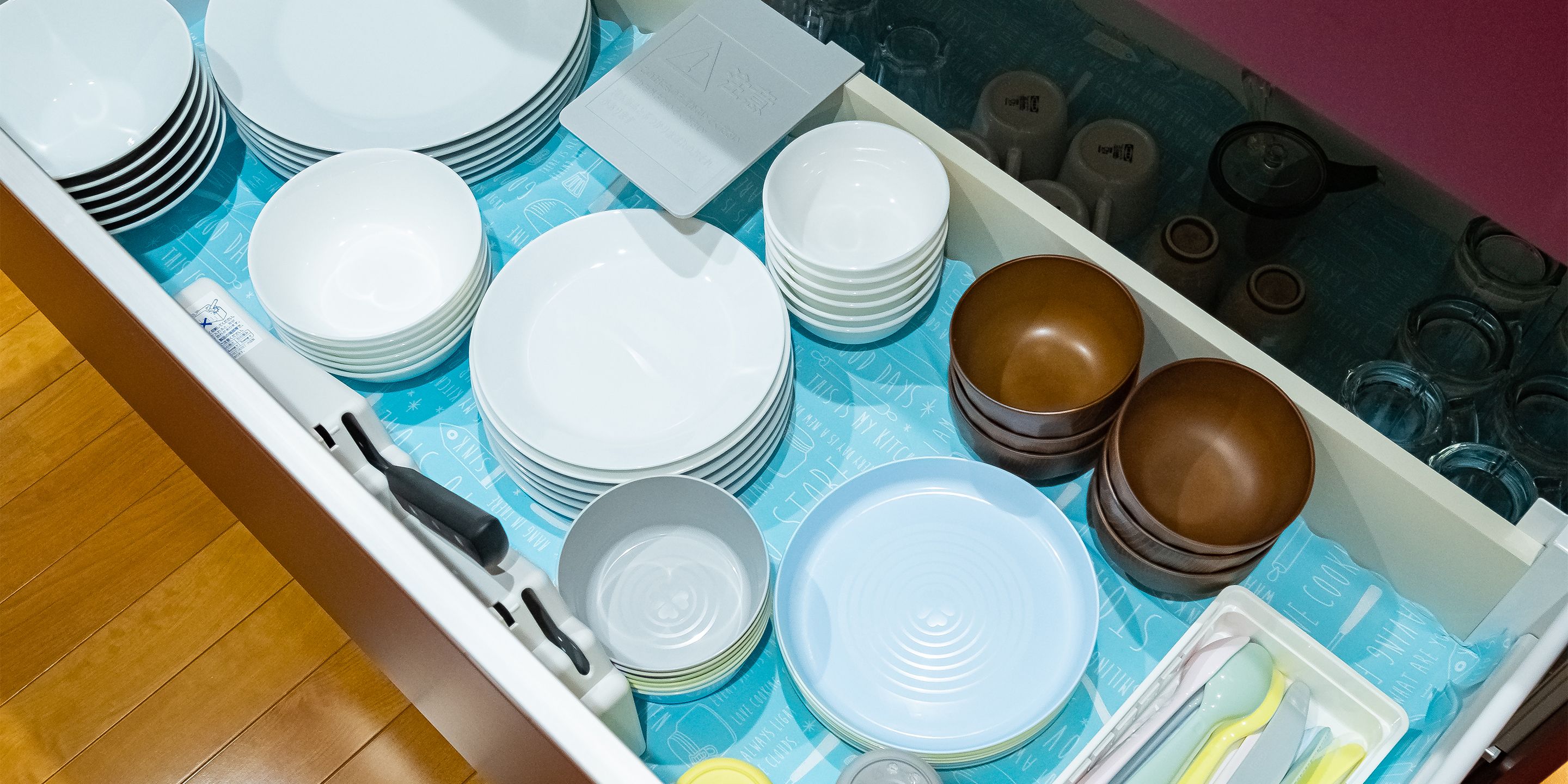 A kitchen drawer with various plates, bowls, and utensils.