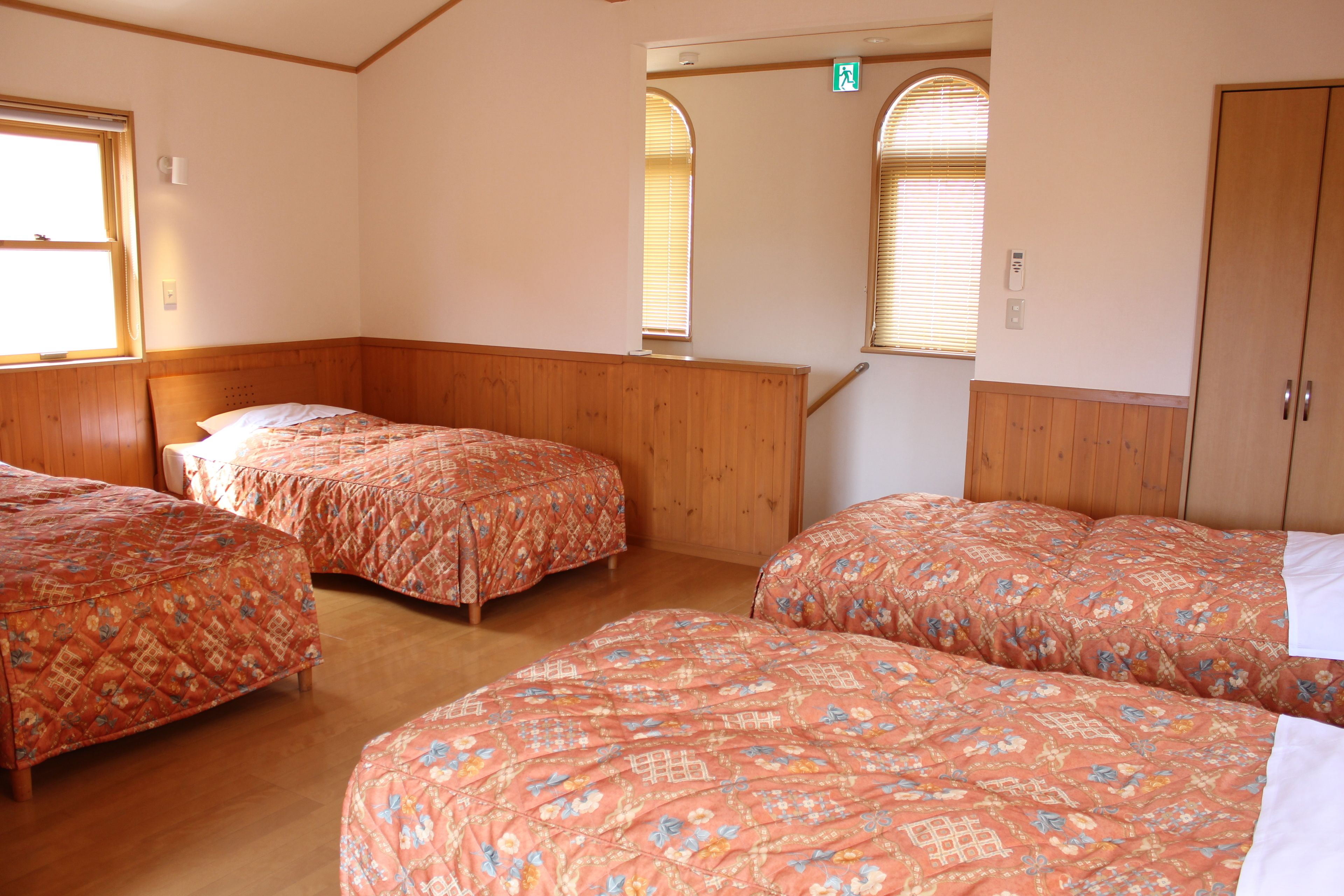 Habitación con tres camas, paneles de madera y una escalera que sube a un nivel superior.