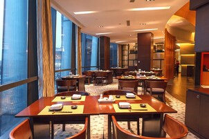 A hotel dining area with multiple tables and chairs, large windows, and a modern interior design.