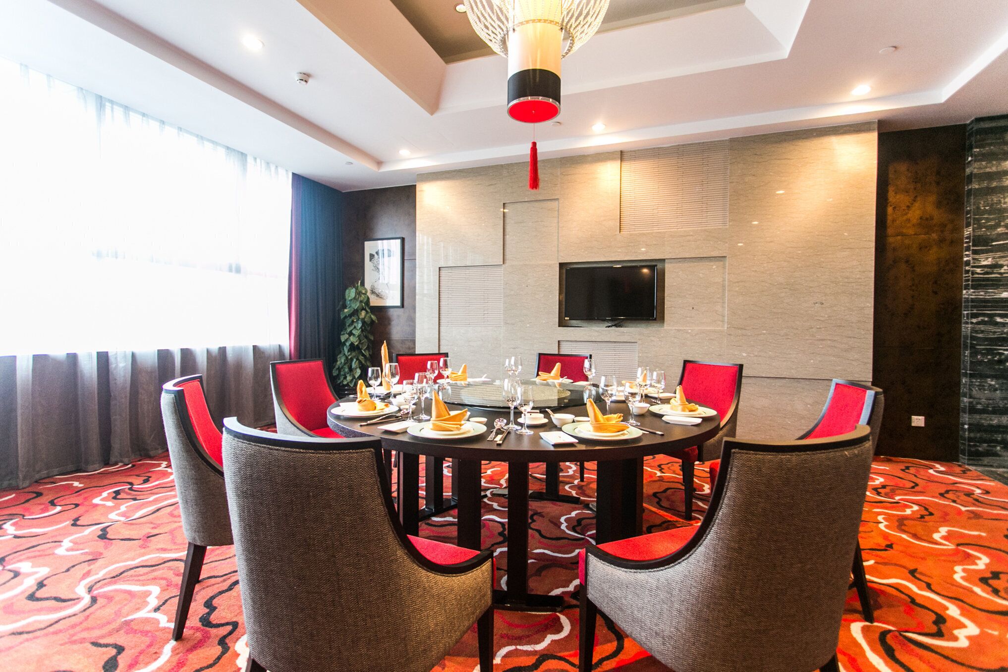 A conference room with a round table set for a meeting, surrounded by chairs with red cushions.