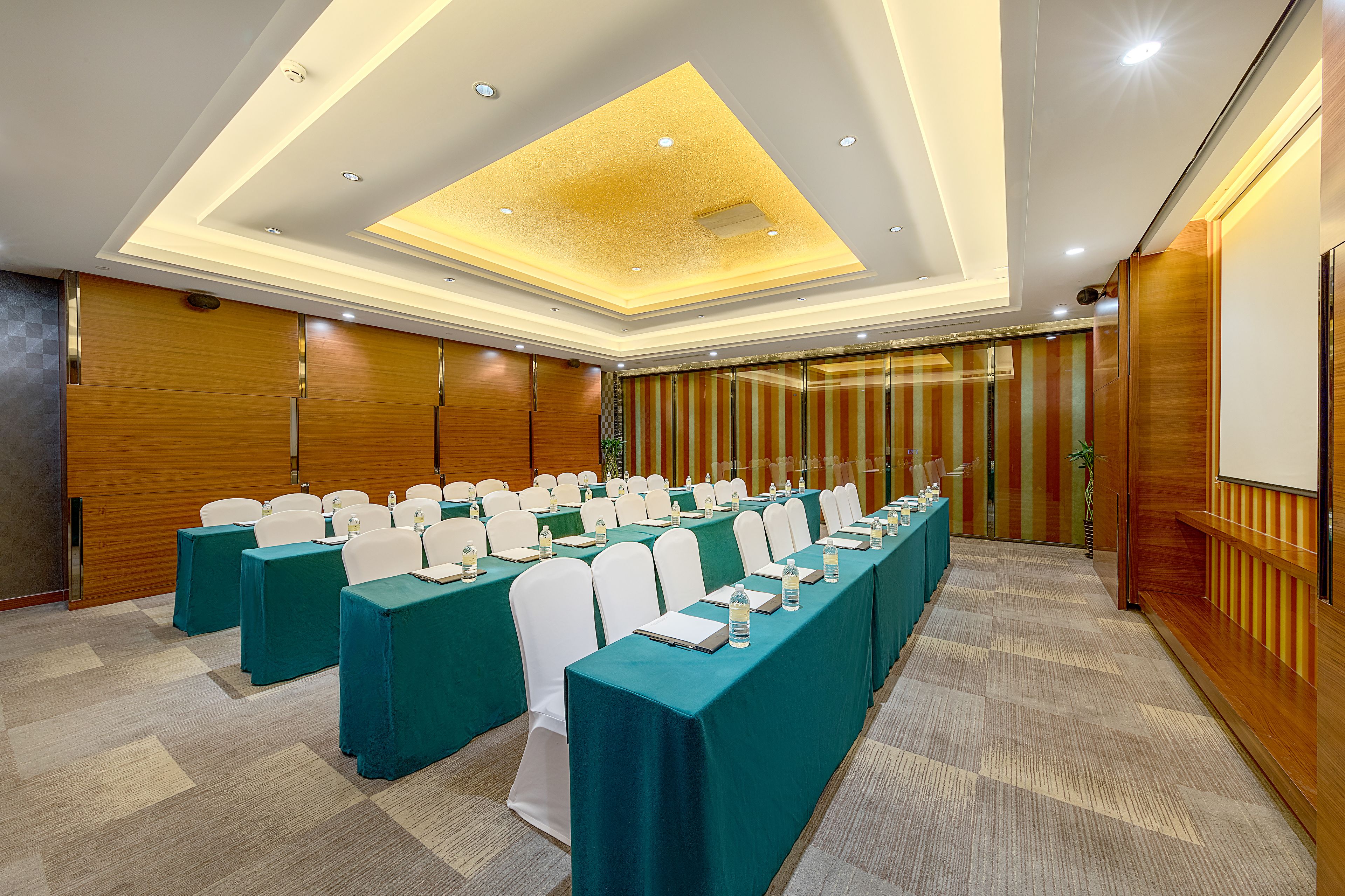 A conference room with rows of tables, white chairs, teal tablecloths, and a wooden panel wall.